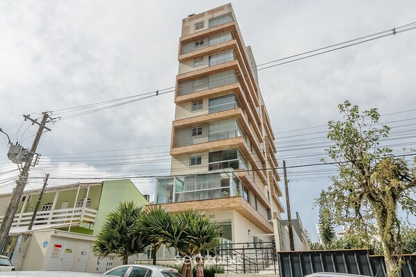 Un immeuble à plusieurs étages, doté de balcons, d’une façade verdoyante et d’un palmier au premier plan.