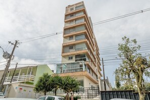Um edifício com várias andares, varandas, fachada verde e uma palmeira em primeiro plano.