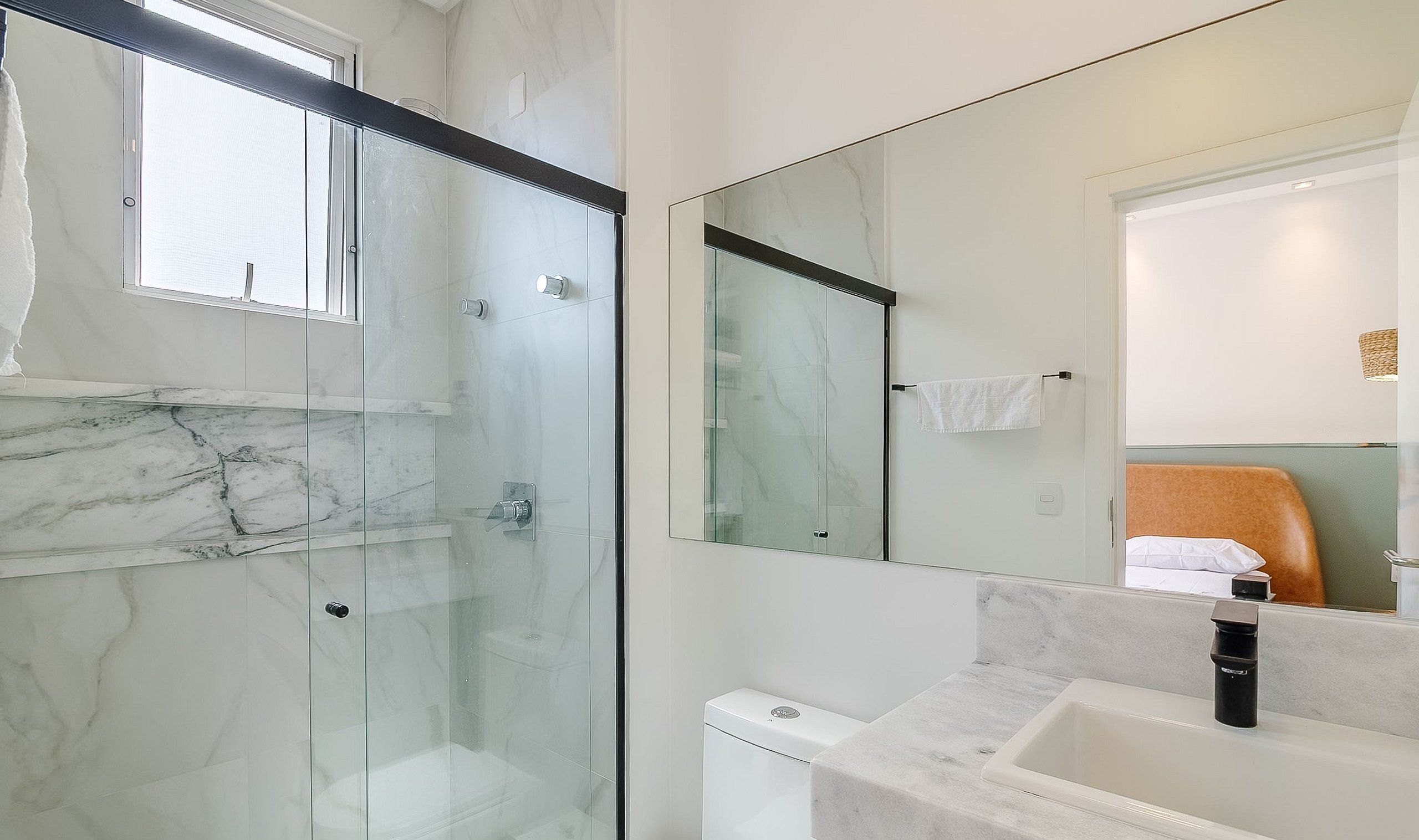 Un baño moderno con cabina de ducha de vidrio, piso de mármol, inodoro blanco y lavamanos con grifo negro.