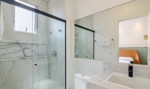 Une salle de bain moderne avec une douche à parois de verre, un sol carrelé en marbre, des toilettes blanches et un lavabo avec un robinet noir.