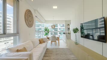 Uma sala de estar moderna com sofá, área de jantar e TV na parede.