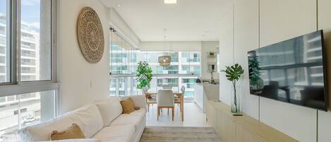 A modern living room with a sofa, a dining area, and a TV mounted on the wall.