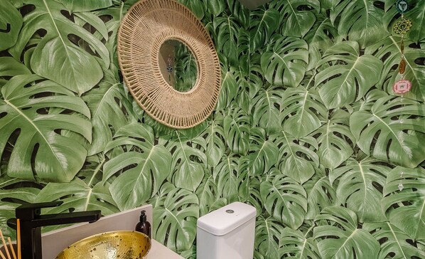 A room with a wall covered in artificial green leaves, a woven basket, a glass bowl, and a white device on a stand. - Apartment w/ Barbecue 240m From the Beach Ehi0401 (Itajai)