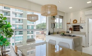 A modern kitchen with a large island, white cabinetry, and a view of a building through large windows. - Apartment w/ Barbecue 240m From the Beach Ehi0401 (Itajai)