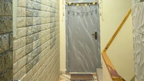 A narrow hallway with a stone-textured wall, a white sink, a marble door, and a ceiling with recessed lighting. - GOPINATH .P GUEST HOUSE (Varanasi)