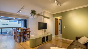 Una sala moderna con comedor, un televisor de pantalla plana montado en la pared y un ventanal con vistas al exterior.