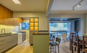 Uma cozinha moderna com uma ilha central, uma área de refeições com cadeiras e uma mesa, e vista para a varanda.