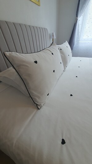 A bed with white bedding and black heart patterns, a grey upholstered headboard, and a bedside lamp.