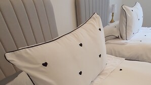 Hotellihuone, jossa on kaksi sänkyä, ja molemmissa on valkoiset vuodevaatteet sekä sydänkuvioidut tyynyt.