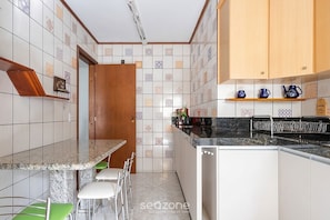 Une cuisine dotée d’un plan de travail en granit, de chaises blanches, d’une porte en bois et de carreaux décorés.