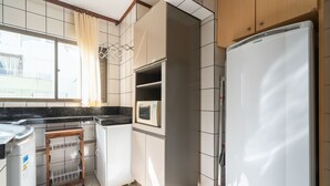 A kitchen with a refrigerator, microwave, and a small shelf unit. - Apartment in Great Location in Meia Praia Eio6031 (Itapema)