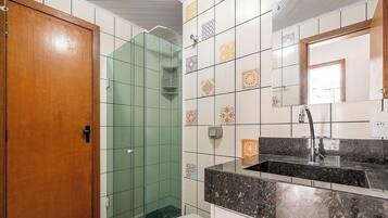 A bathroom with a wooden door, a glass shower enclosure, a tiled wall with patterned tiles, and a sink with a marble countertop.