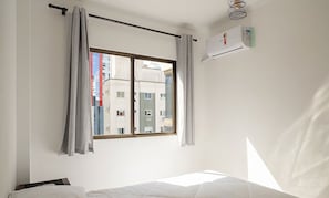 Une chambre avec une fenêtre, un lit, des rideaux et un appareil de climatisation.
