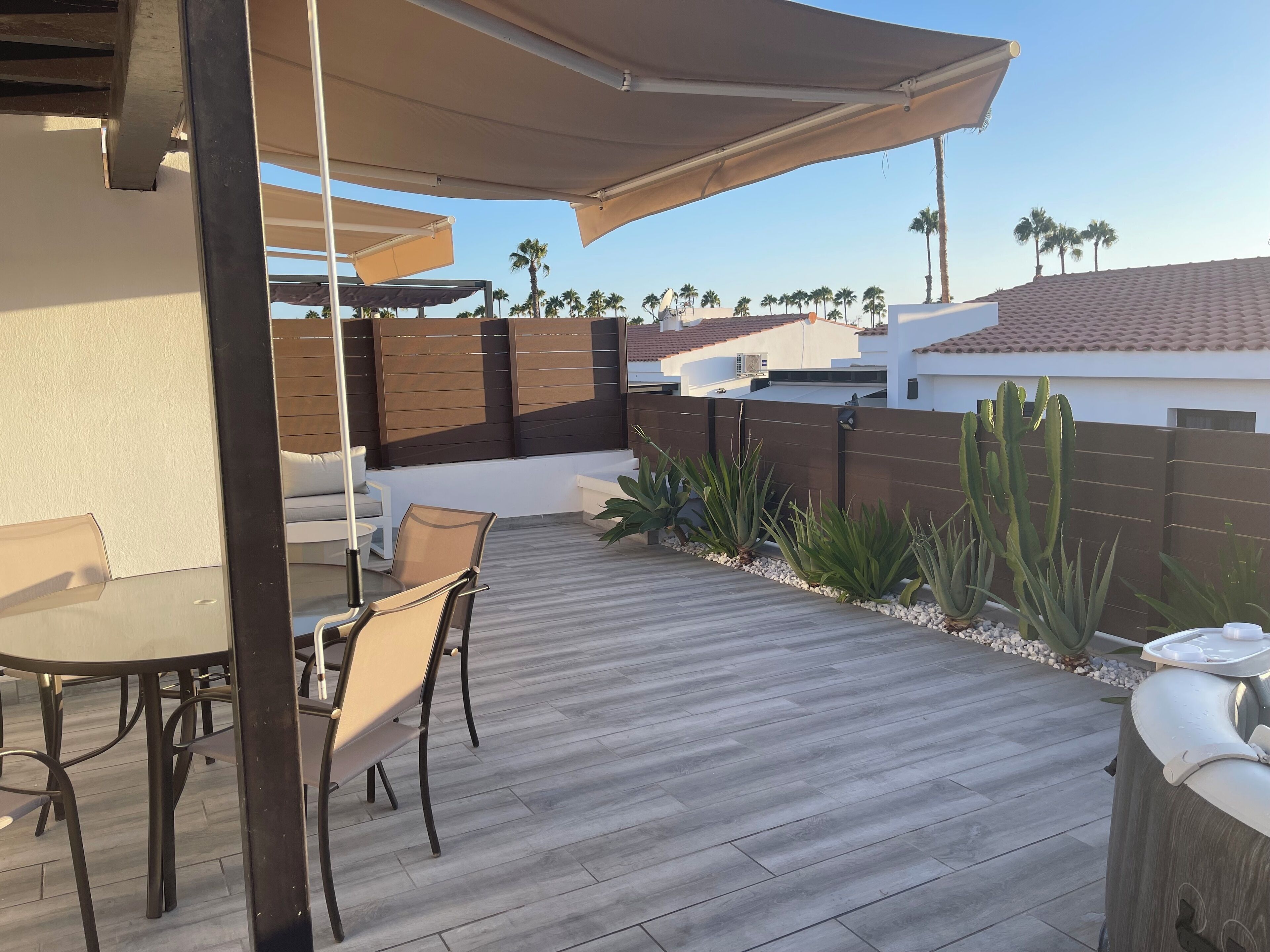 An outdoor patio with a wooden deck, a table with chairs, and a large umbrella providing shade.