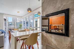 Une cuisine moderne dotée d’un meuble à vin intégré, de grandes fenêtres et d’un coin repas avec une table et des chaises blanches.