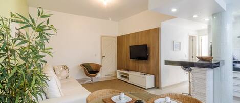 Una sala de estar moderna con un sofá, un televisor y un comedor con una mesa preparada para dos personas.