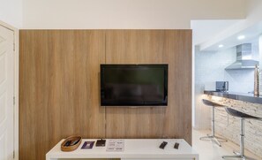 A modern kitchen with a flat-screen TV mounted on a wooden wall, a white countertop, and two bar stools.