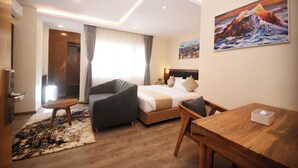 A modern hotel room with a bed, a desk, a chair, a sofa, and a painting on the wall.