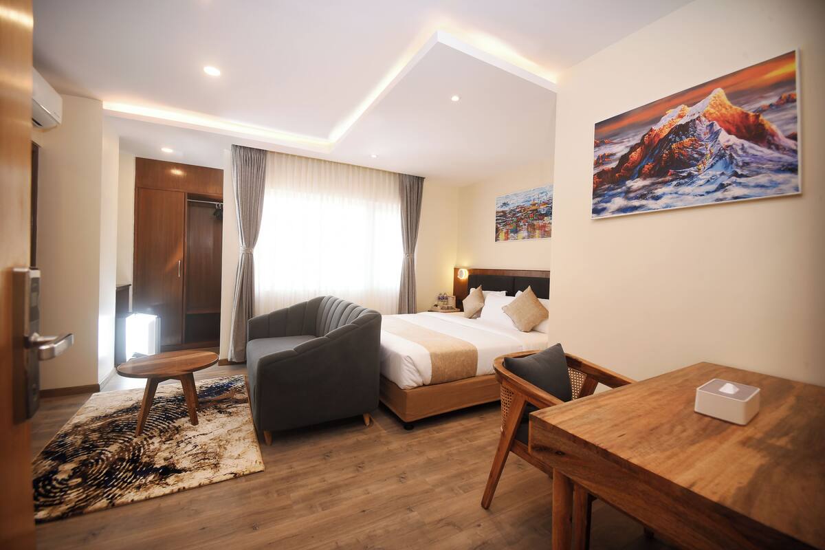 Una habitación de hotel moderna con una cama, un escritorio, una silla, un sofá y un cuadro en la pared.