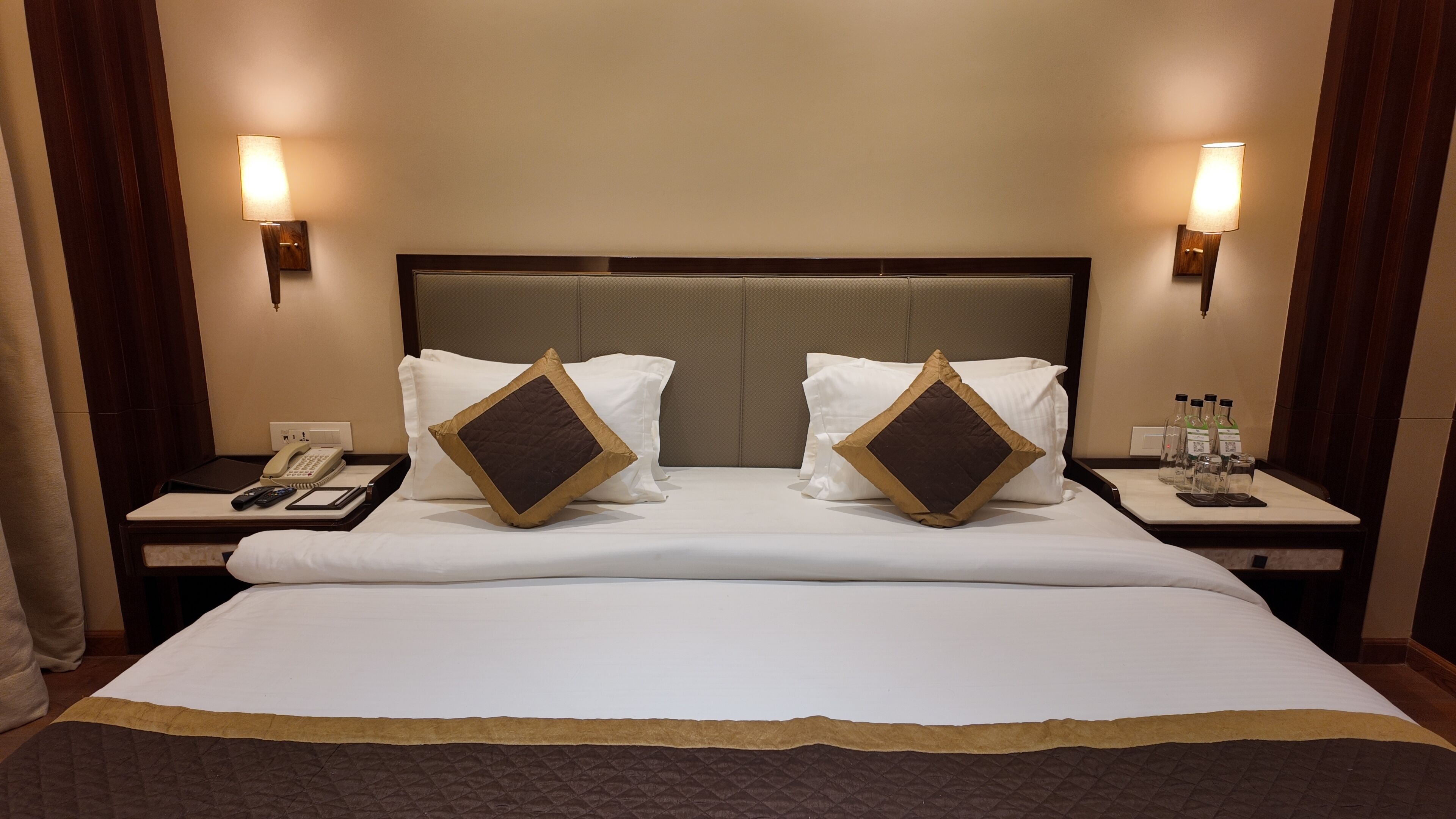 Una habitación de hotel con una cama grande, dos mesitas de noche, un teléfono y un minibar.