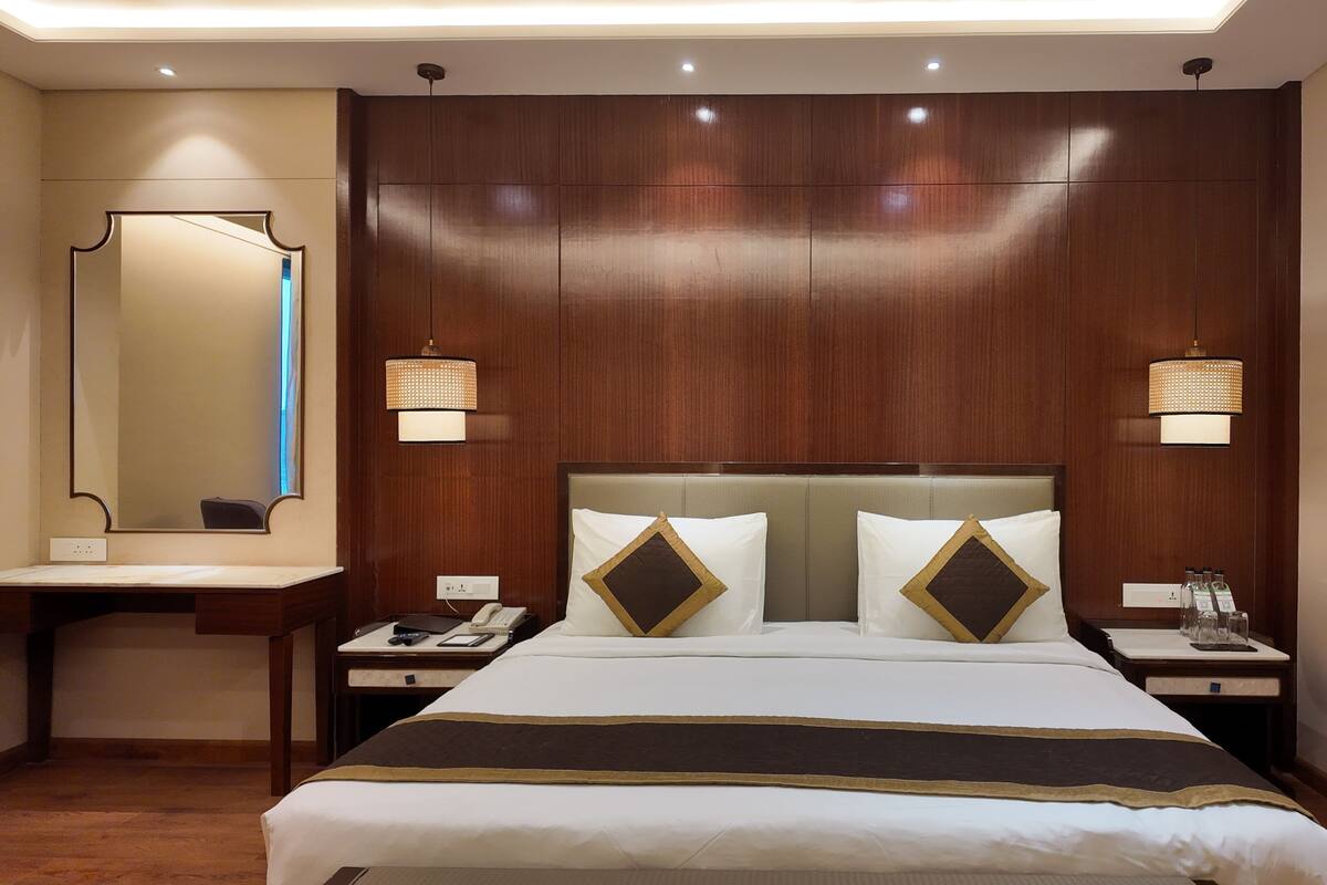 A hotel room with a large bed, two bedside tables, a nightstand, a mirror, and a wall-mounted lamp.