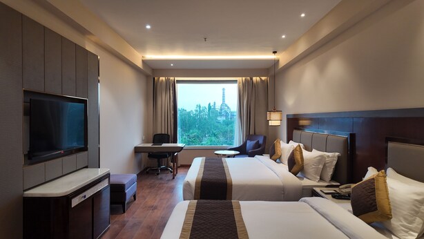 Hotelkamer met twee bedden, een bureau, een televisie en een groot raam met uitzicht op een toren.