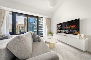 A modern living room with a large window, a sofa, a coffee table, a TV, and a white cabinet.