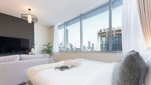 Moderni hotellihuone, jossa on suuri sänky, sohva, televisio ja näkymä kaupunkiin.