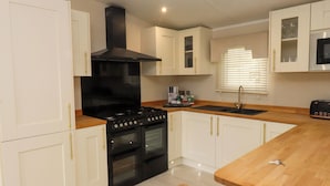 A modern kitchen with white cabinets, a black stove, and a wooden countertop. - The Chalet at Tyn Lon (Pwllheli)