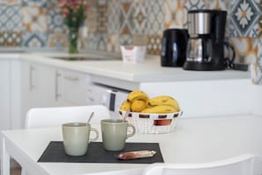 A kitchen with a white countertop, a coffee maker, a basket of bananas, and two mugs.