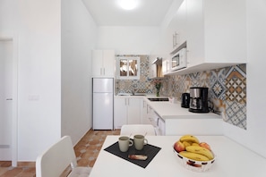 A compact kitchen with white cabinets, a refrigerator, a coffee maker, and a tiled backsplash.