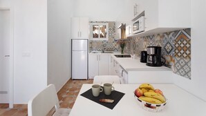 A compact kitchen with white cabinets, a refrigerator, a coffee maker, and a tiled backsplash.
