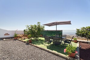 Un patio con una mesa, sillas, un paraguas y plantas en macetas.