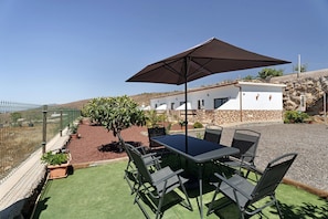 Un patio al aire libre con una mesa y sillas, un parasol grande y vistas a un edificio blanco de fachada de piedra.