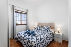 A bedroom with a bed, a nightstand, a window with curtains, and a headboard.