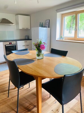 Un comedor con una mesa redonda de madera, sillas negras y un florero con flores.