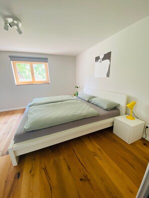 Un dormitorio con cama, mesita de noche, lámpara, ventana y una obra de arte en la pared.