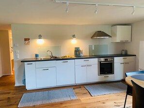 Una cocina moderna con gabinetes blancos, estufa de acero inoxidable y horno empotrado.