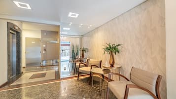 Um saguão de hotel com piso de mármore, balcão de recepção, área de estar e parede com padrão.