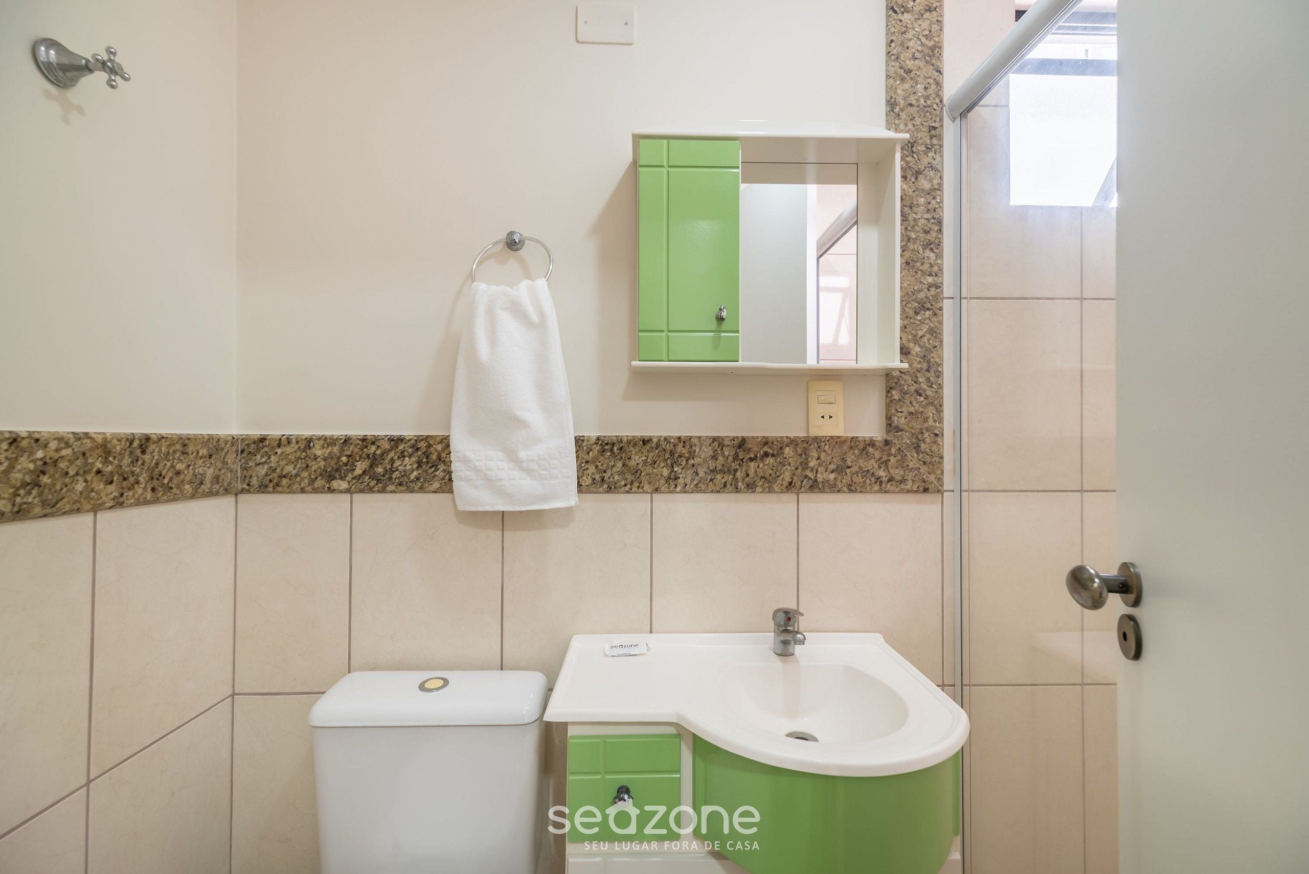 A bathroom with a toilet, sink, green cabinet, and a towel hanging on the wall.