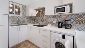 Una cocina compacta con armarios blancos, microondas integrado, cafetera y lavadora.