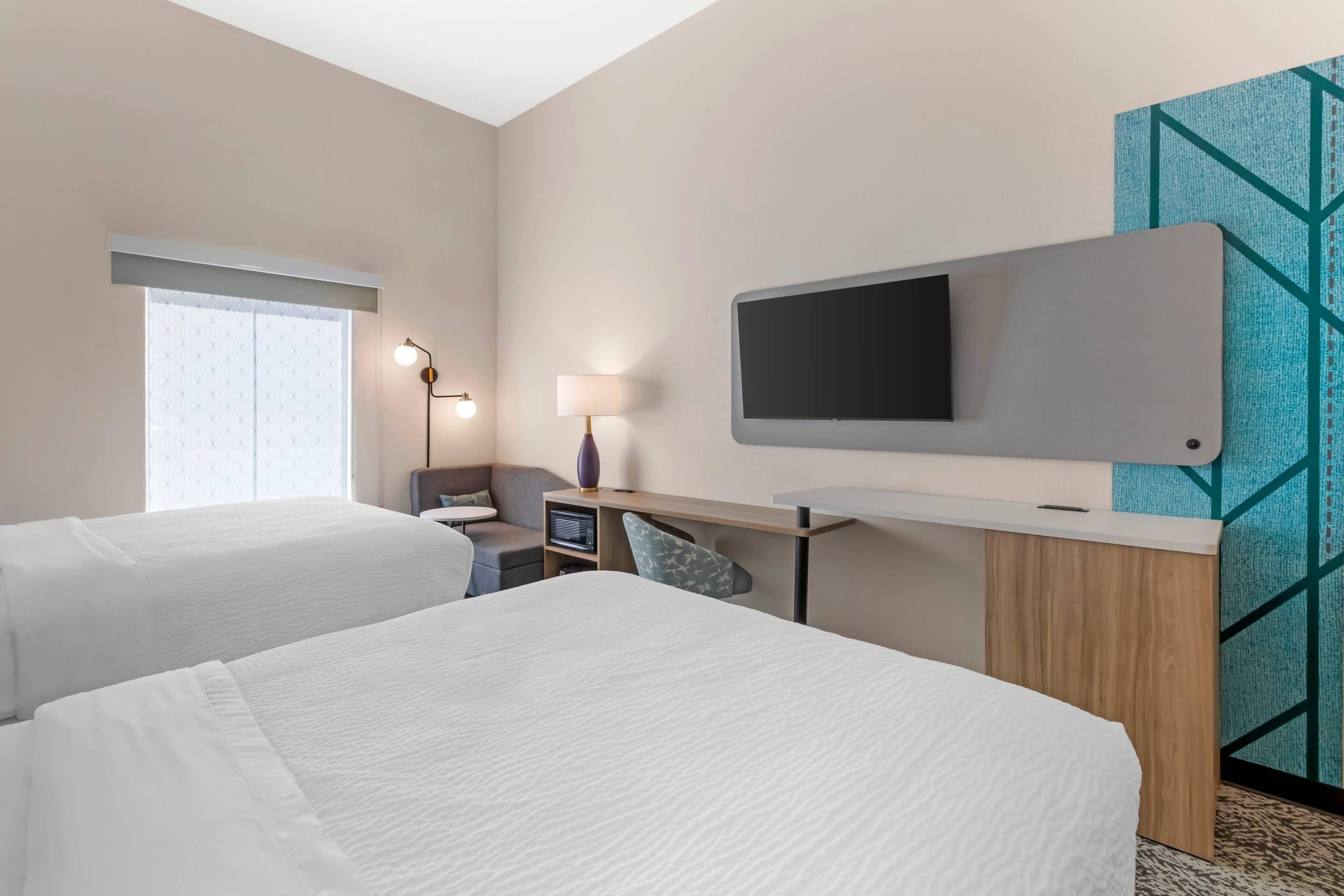 Habitación de hotel con dos camas, un escritorio con computadora, televisión y ventana con persianas.