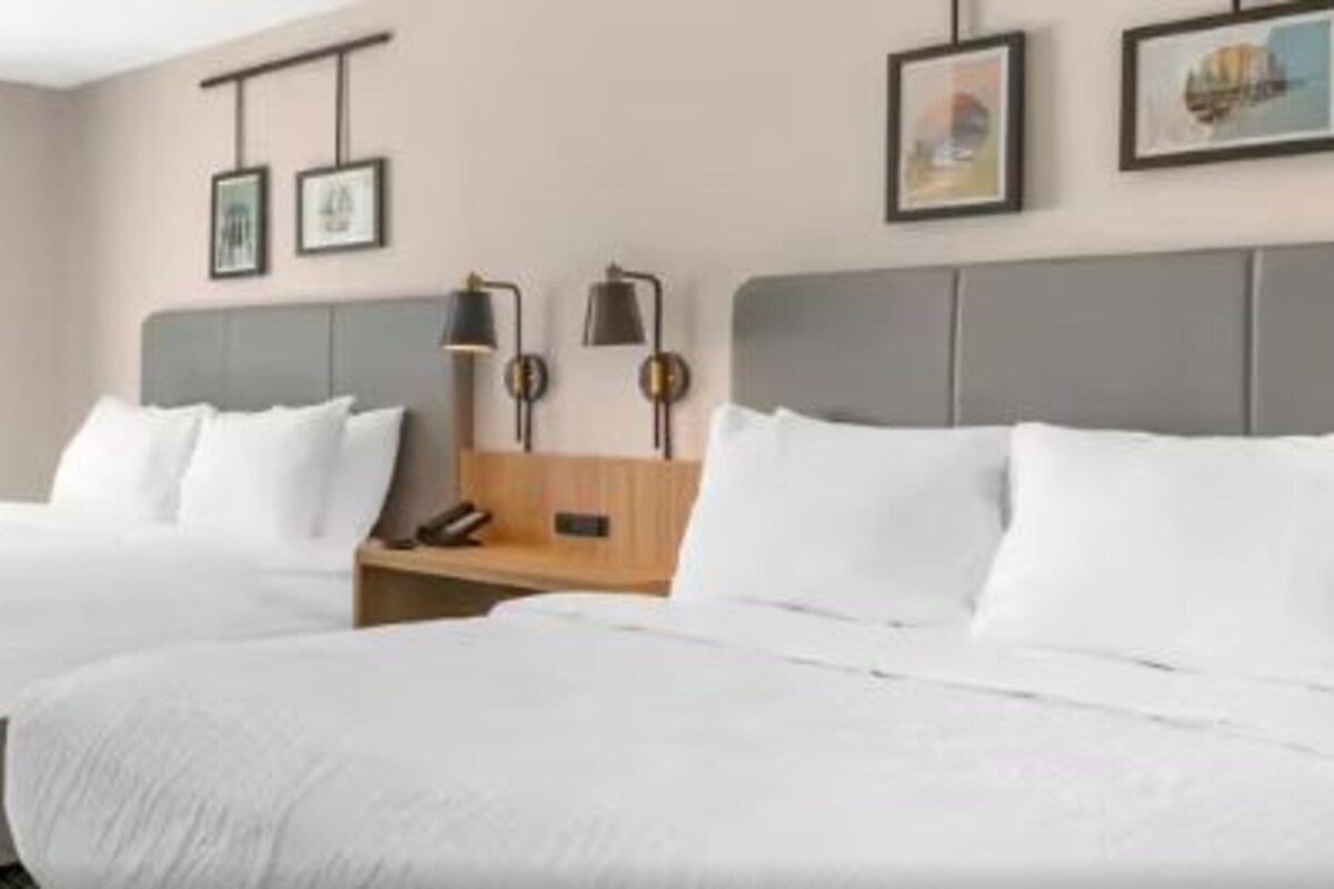 A hotel room with two beds, a small table, a chair, a desk, and a window with curtains.