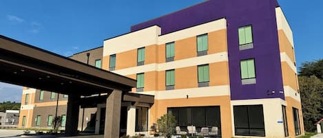 Un immeuble à plusieurs étages, doté d’une façade violette, de grandes fenêtres et d’un espace d’entrée abrité.