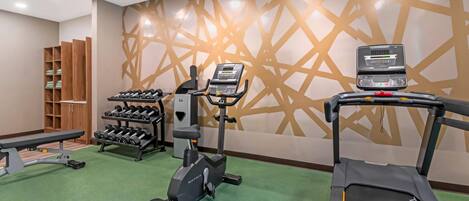 A gym with exercise equipment including a treadmill, elliptical, and dumbbells.