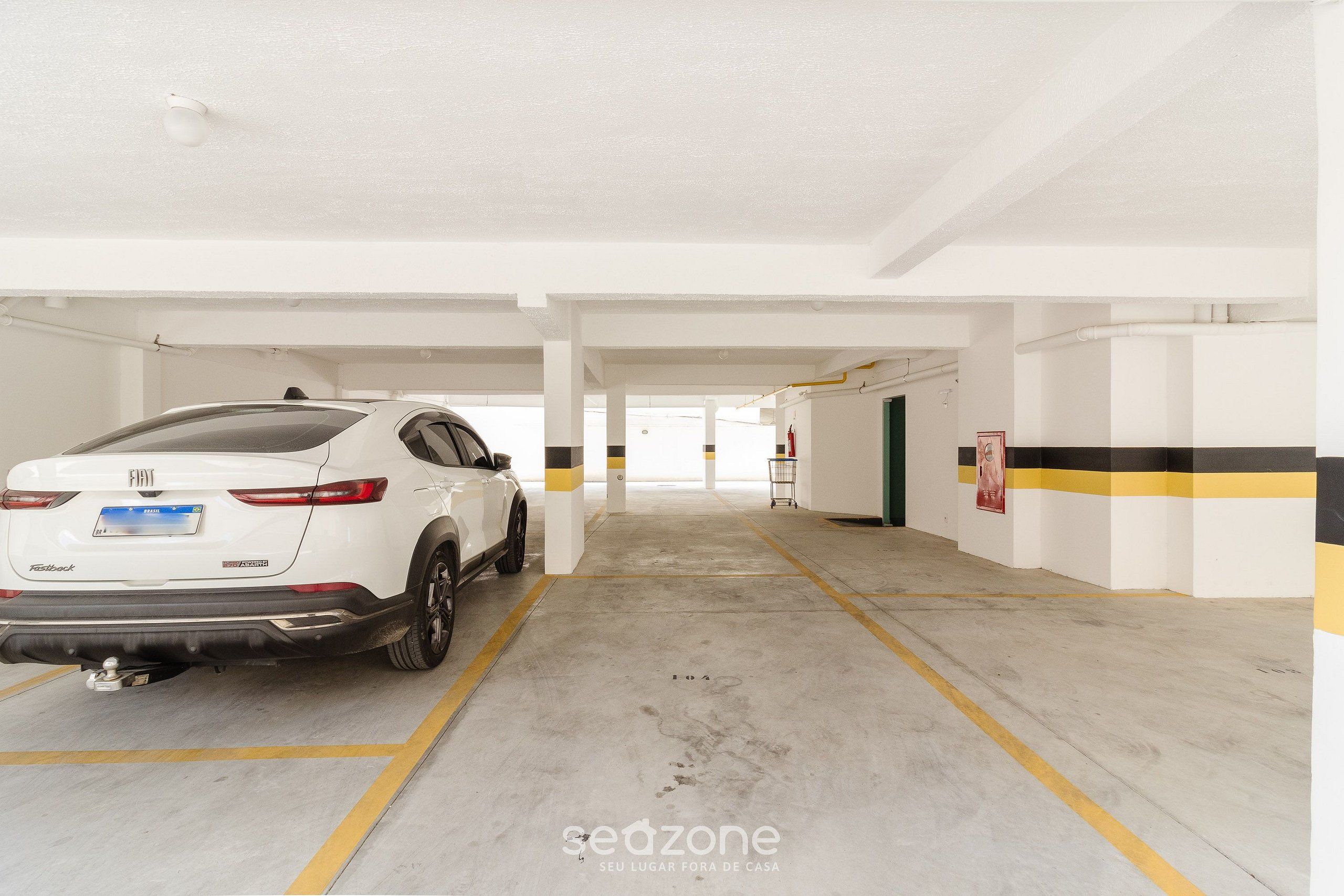 Ein weißer SUV steht in einer Tiefgarage mit weißen Wänden und gelben Markierungen.