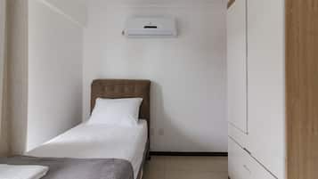 Una habitación pequeña y ordenada con una cama individual, aire acondicionado de pared y un panel de madera en una pared.