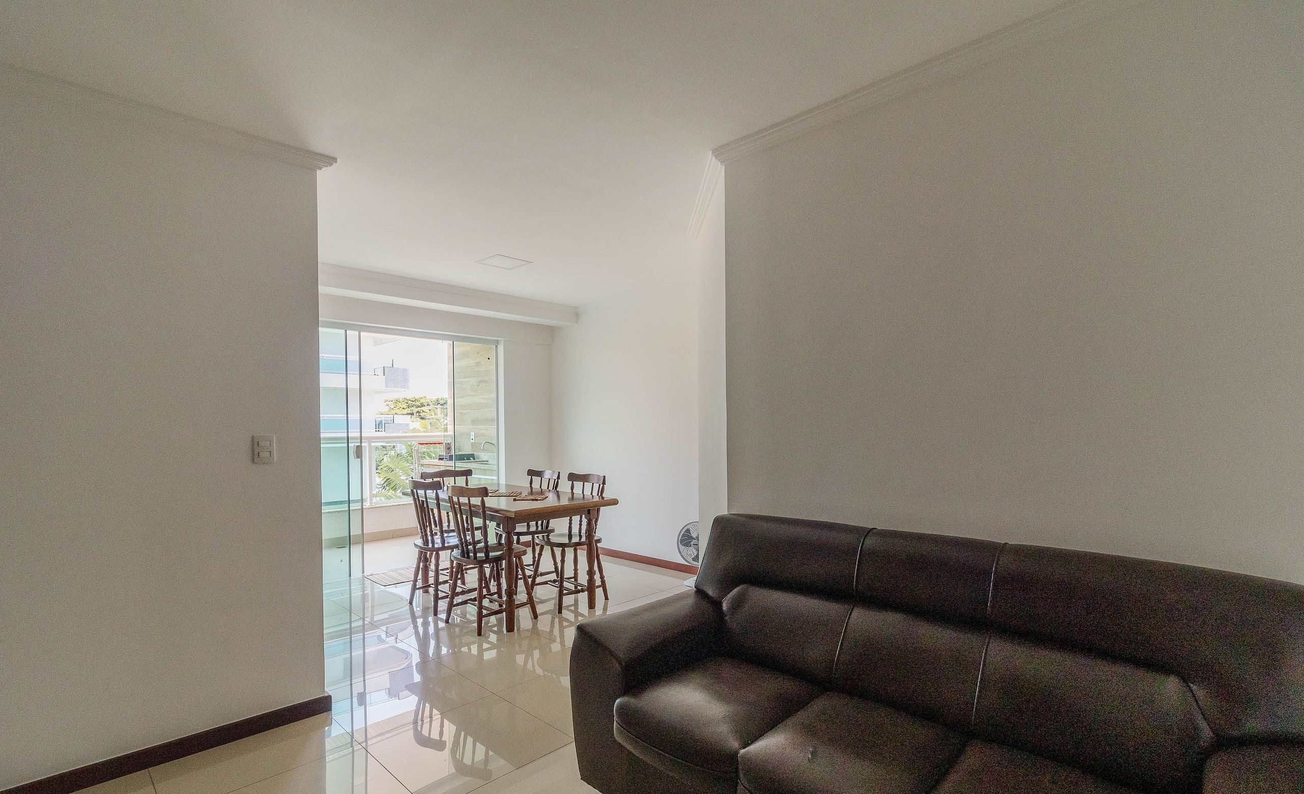 A spacious living area with a leather sofa, a dining table with chairs, and a large window offering a view of the outdoors.