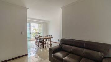A spacious living area with a leather sofa, a dining table with chairs, and a large window offering a view of the outdoors.