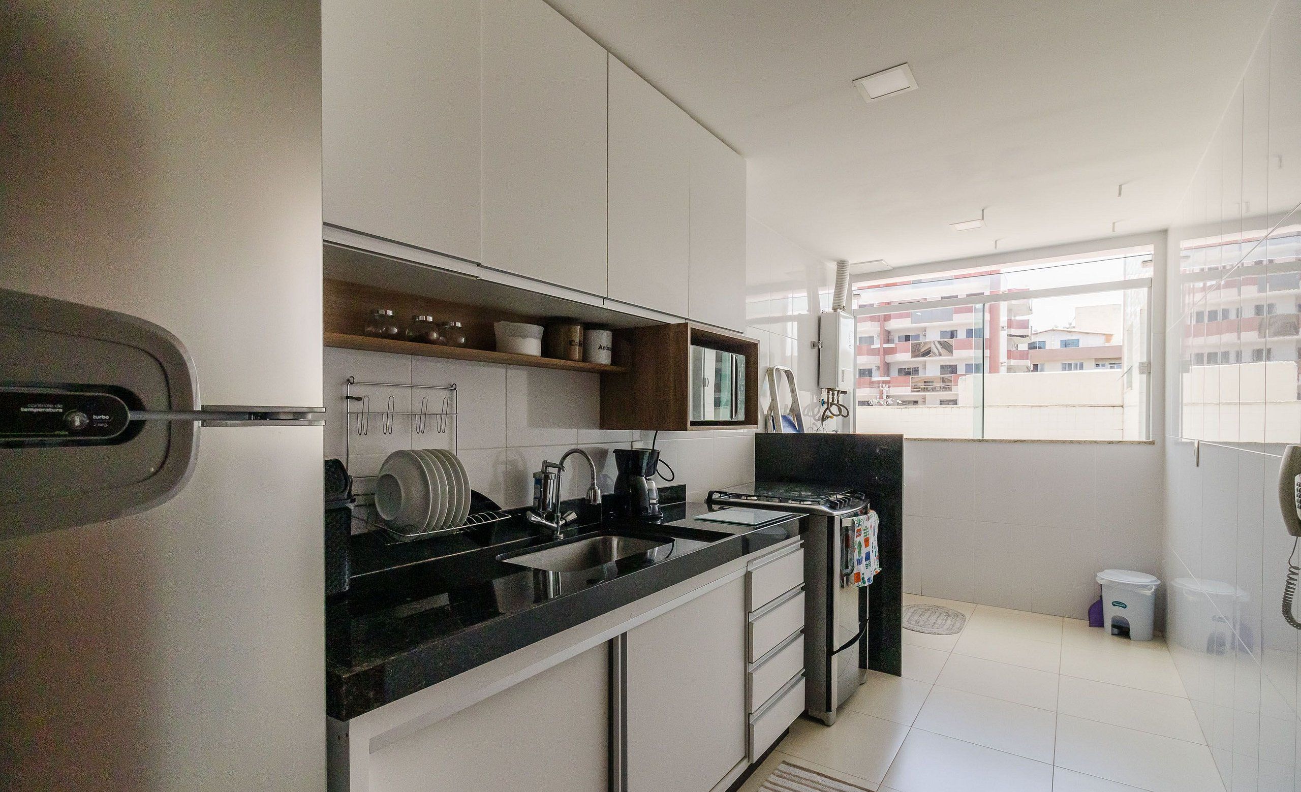 A modern kitchen with white cabinets, a black countertop, and a window with a view of buildings.